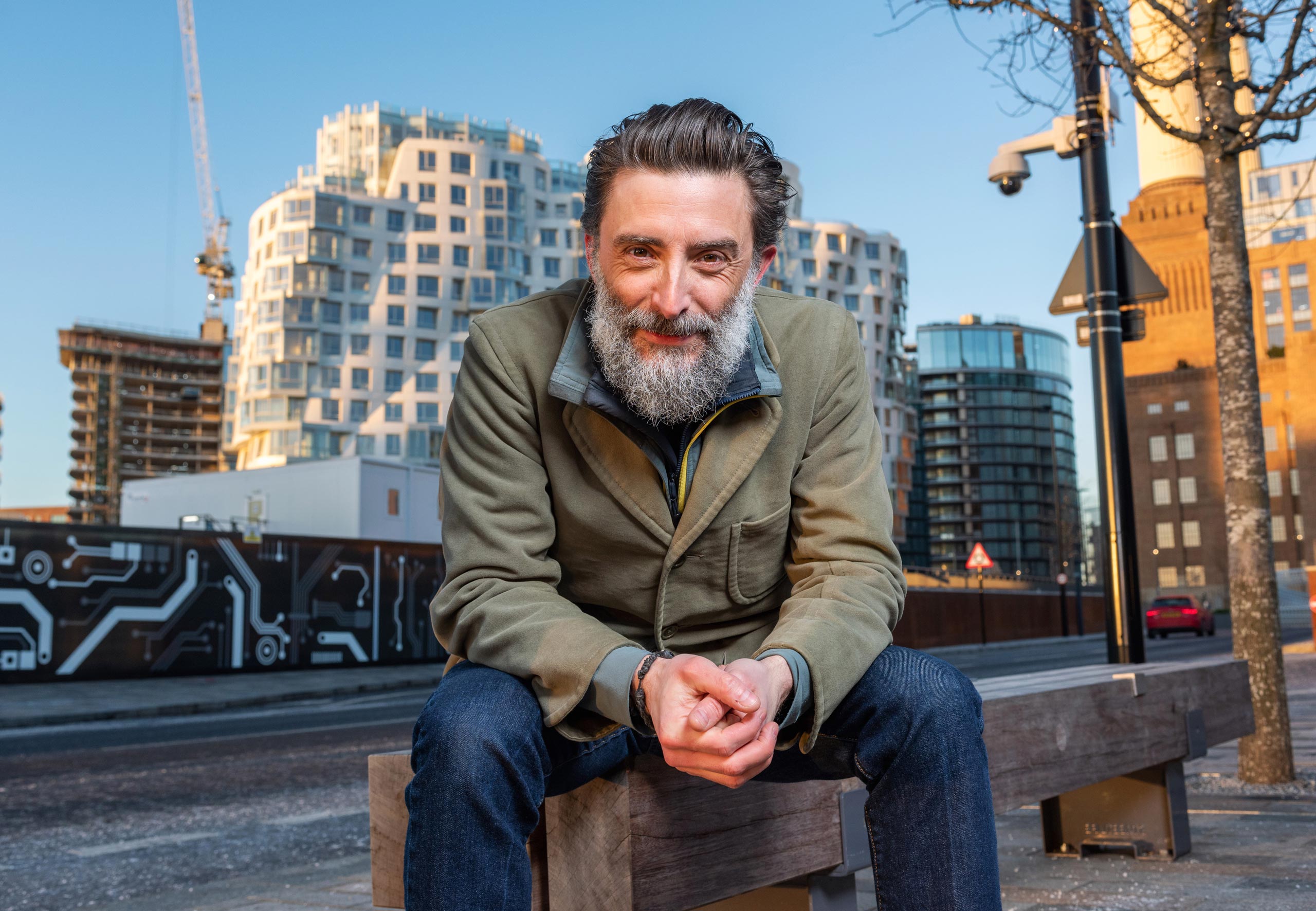 Contemporary business portrait of an architect sitting in a bustling street in London. Dressed in casual attire, he exudes confidence and expertise in his field while maintaining a relaxed and approachable demeanor. The city's iconic architecture serves as a fitting backdrop for this image of a successful professional.