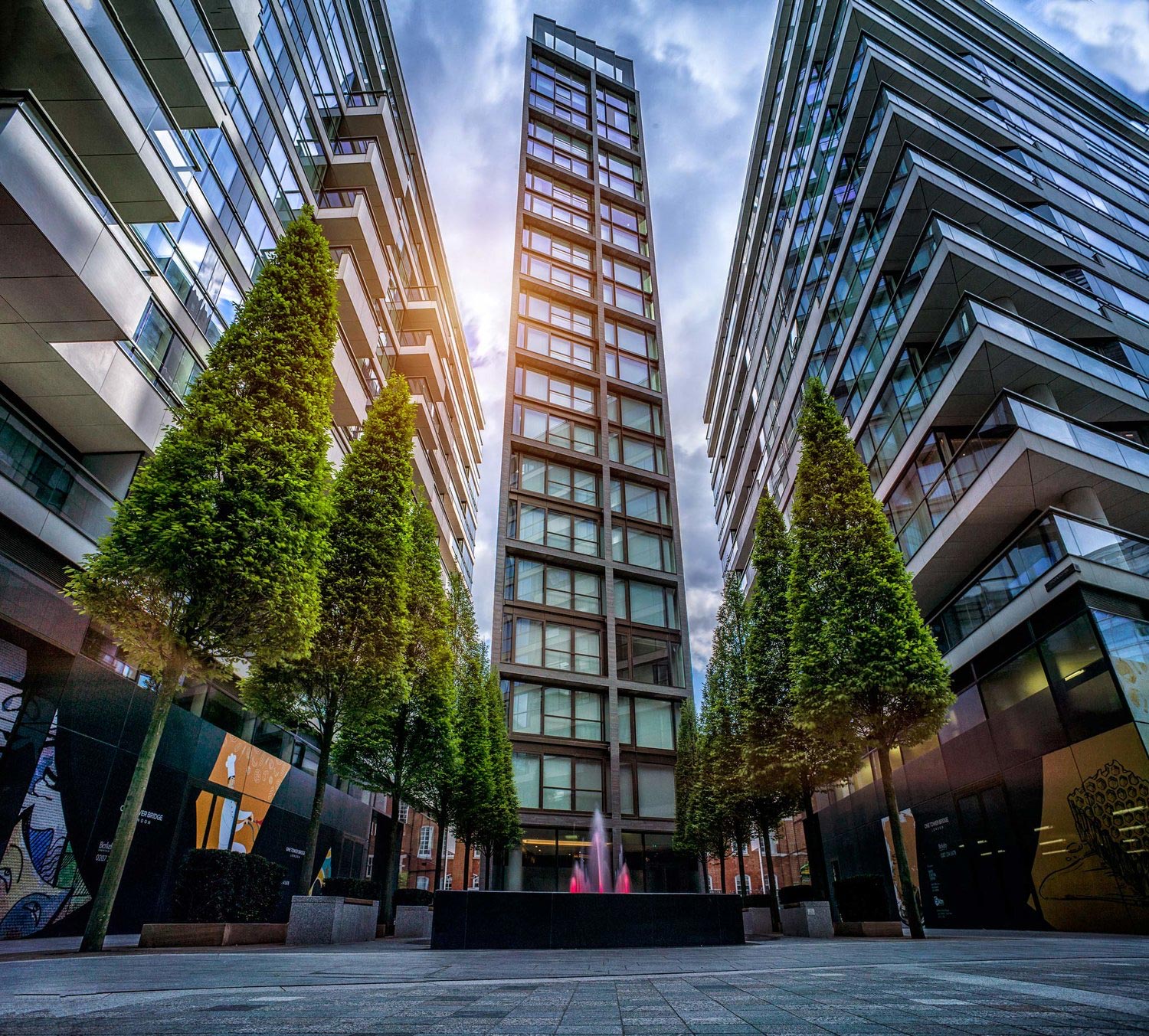 Low-angle shot of a modern apartment building near Tower Bridge, captured by Wright Content. The glass-fronted tower rises against a backdrop of green trees.