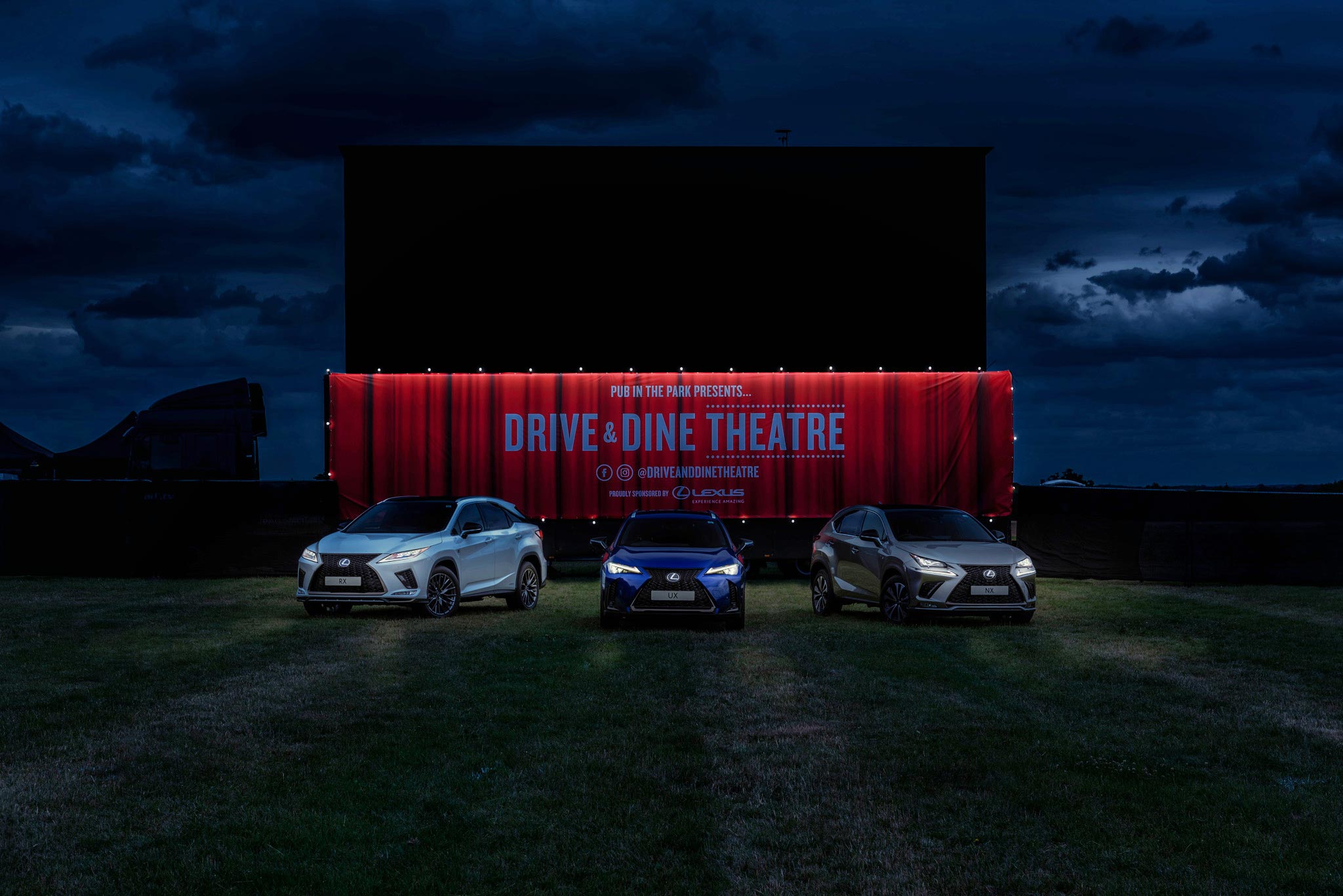 A promotional shot for a Lexus event, showcasing an open-air cinema premiere at night. Three Lexus cars are parked in front of a giant cinema screen with a large red curtain, creating a captivating atmosphere with headlights illuminating the dusk scene.