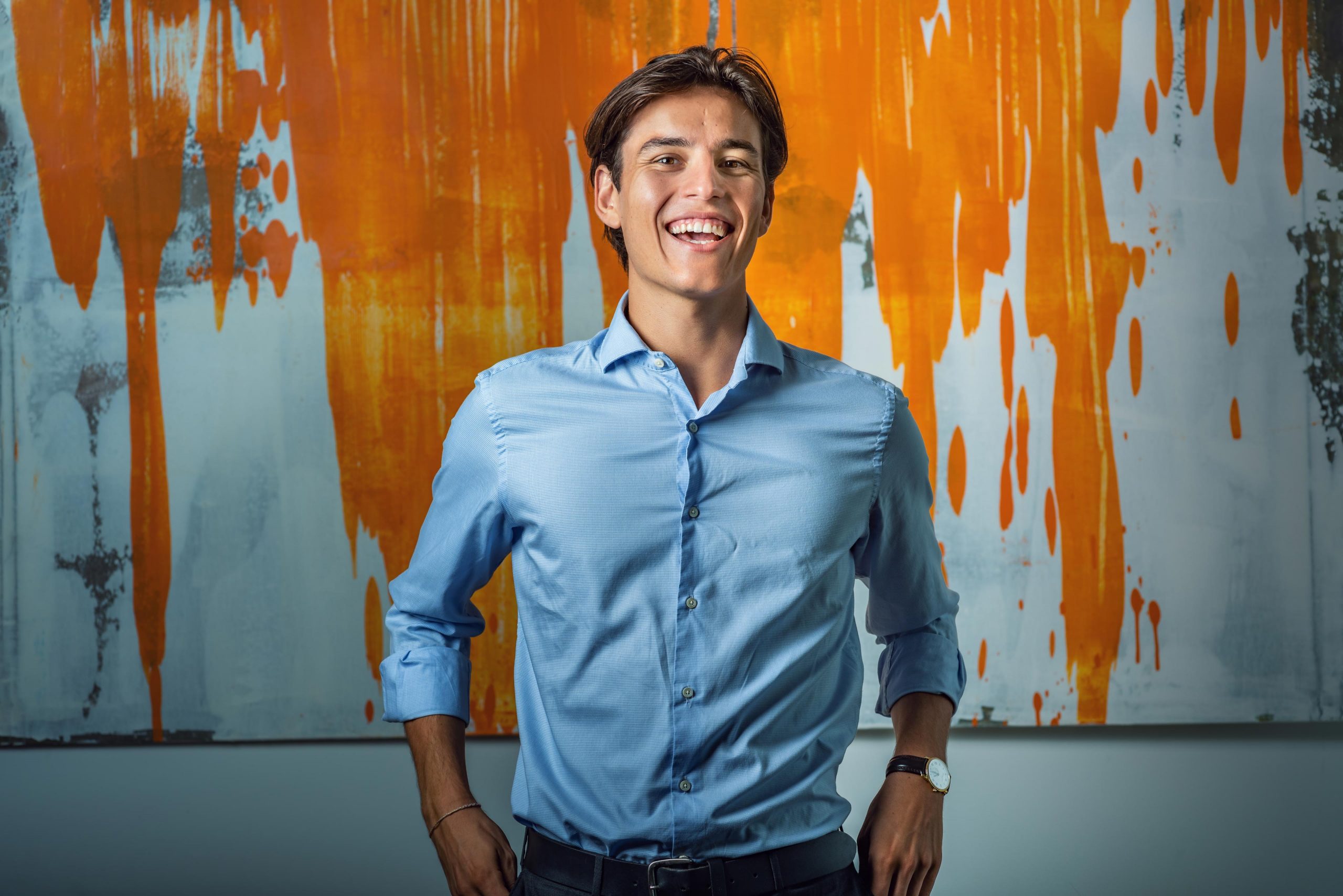 A handsome young man smiles for his LinkedIn professional portrait with beautiful artwork in the background, captured by Wright Content, a LinkedIn headshot photographer in London.