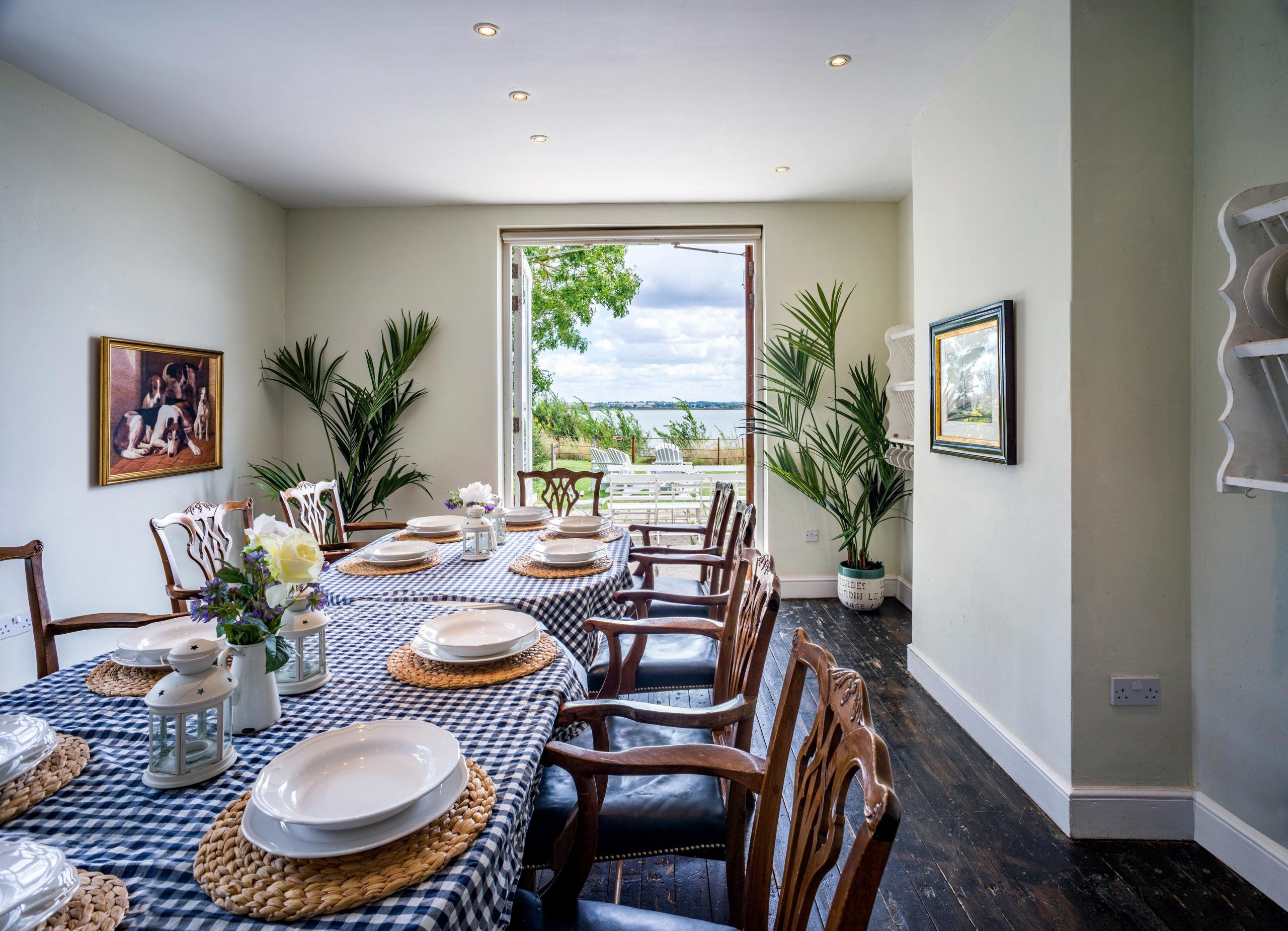 Captivating image of the breakfast room at Osea Island Resort, featuring a large wooden table adorned with flowers, plates, and tableware. French doors open to reveal a stunning view of the private beach and sea, inviting guests to enjoy a scenic breakfast experience.