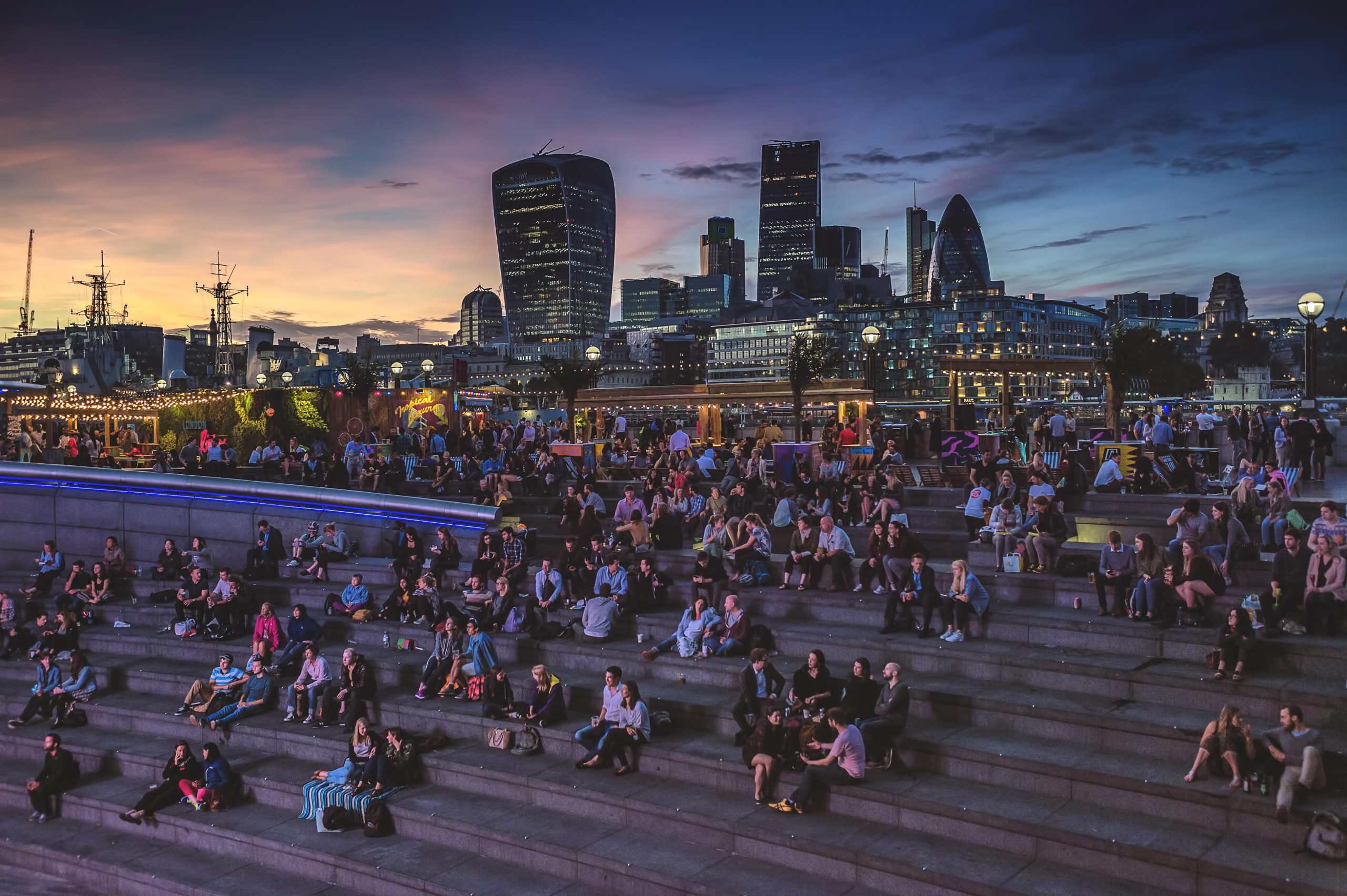 Vibrant nighttime shot of a gathering at The Scoop, captured by Wright Content. People gather for a music event, illuminated by colorful lights, with the London cityscape in the background.