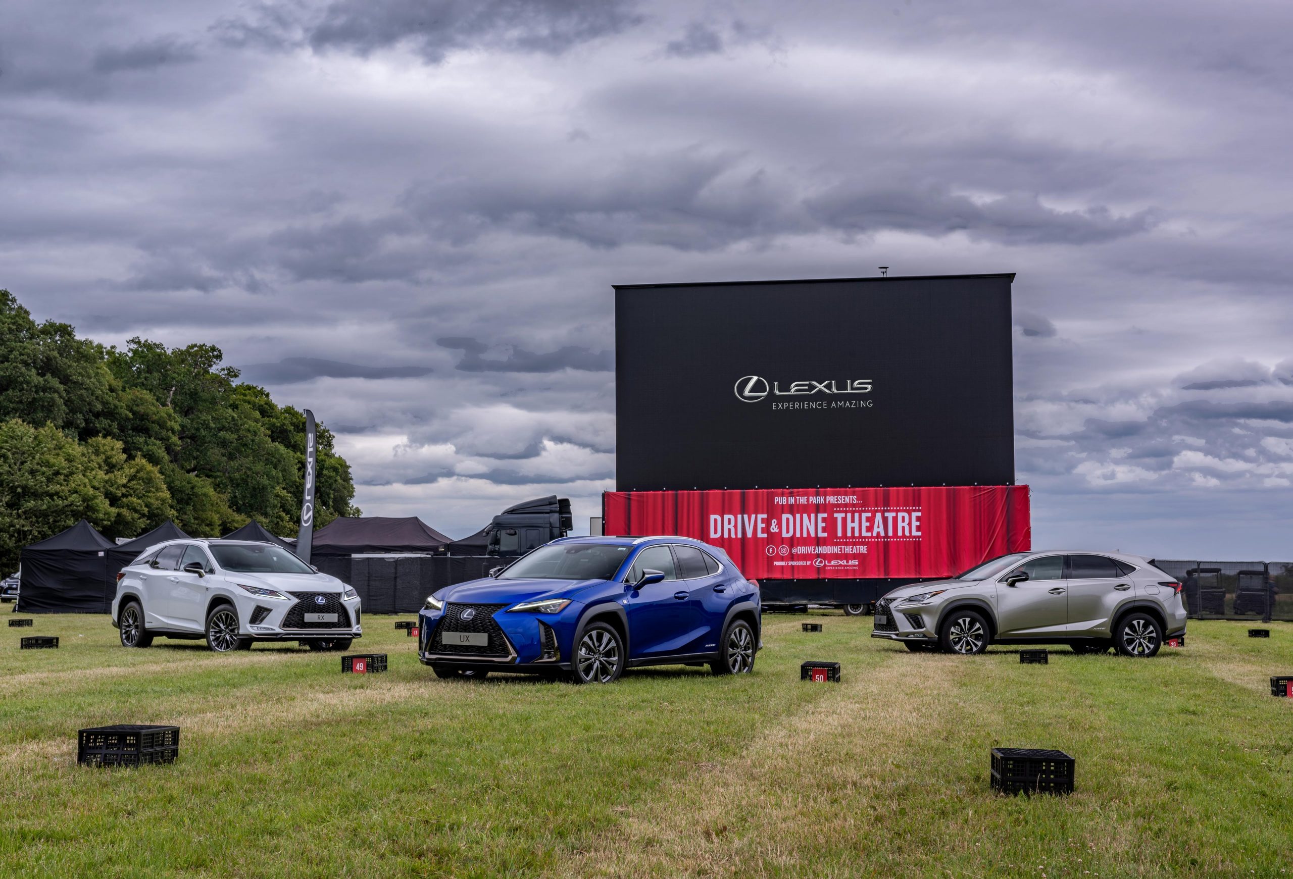 A daytime shot of a Lexus event, featuring cars lined up at angles in front of a giant cinema screen. The scene exudes elegance and anticipation as attendees gather for the open-air cinema experience, captured in stunning detail by Wright Content.