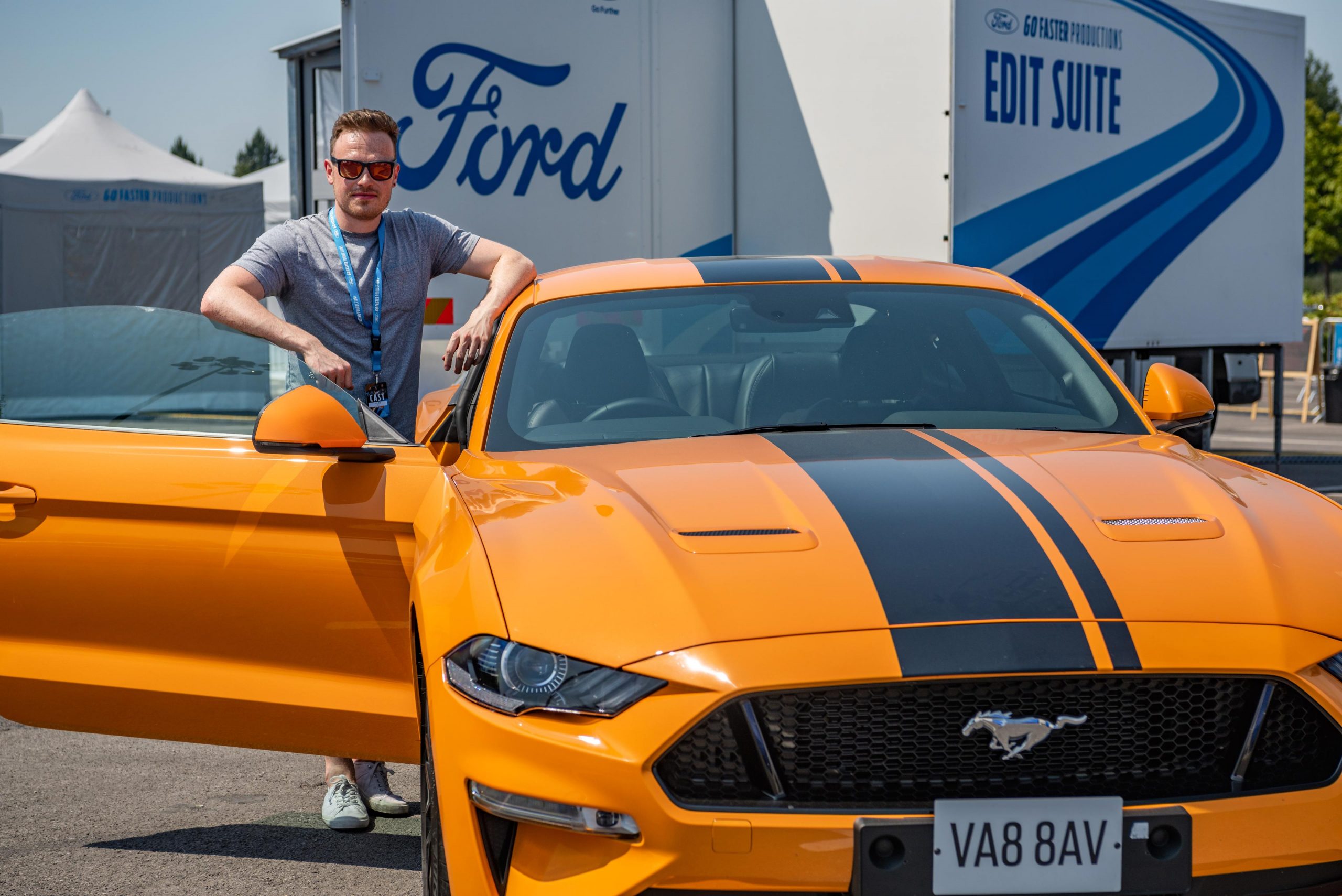 An image captured at a brand event for Ford, featuring a journalist from the press posing next to an orange Mustang. The scene exudes excitement and anticipation as attendees prepare to experience track day thrills, captured in detail by Wright Content.