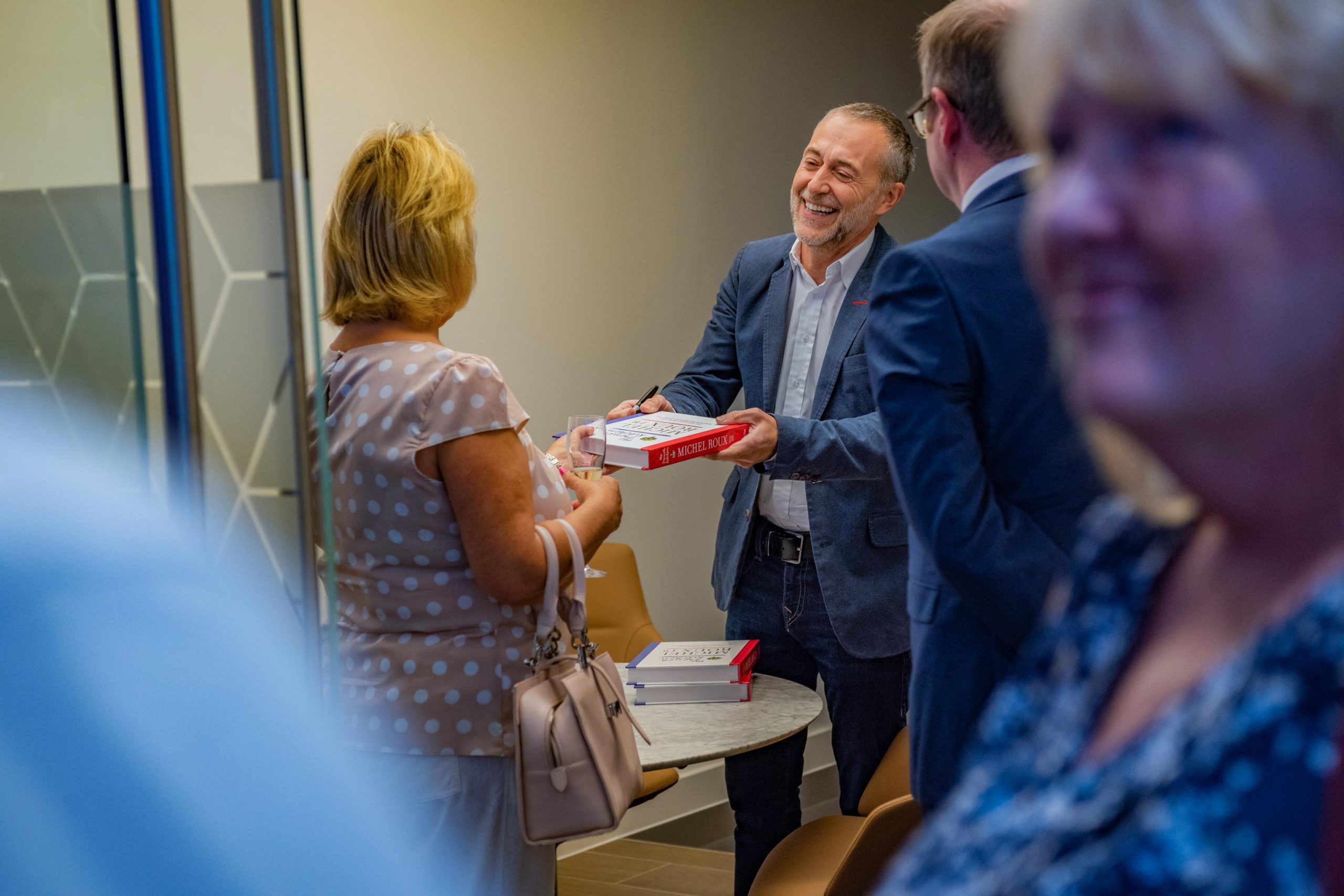Michel Roux, the famous chef, signs books at an event captured by Wright Content. In this reportage-style photograph, he hands a signed book over to a woman.