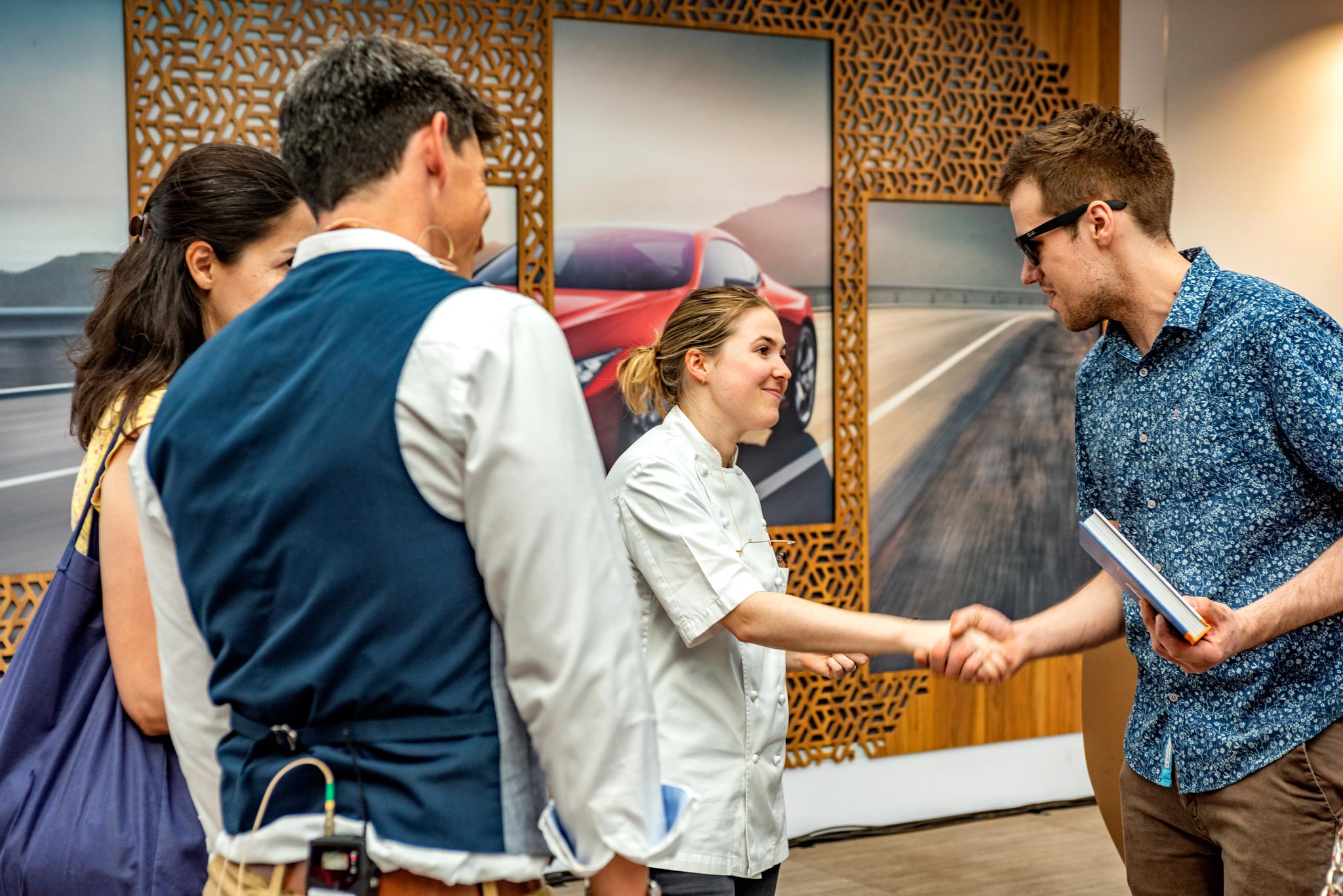 Emily Roux, the famous chef, hands over a signed copy of her book to a customer at an automotive event for Lexus, captured in a reportage style by Wright Content.
