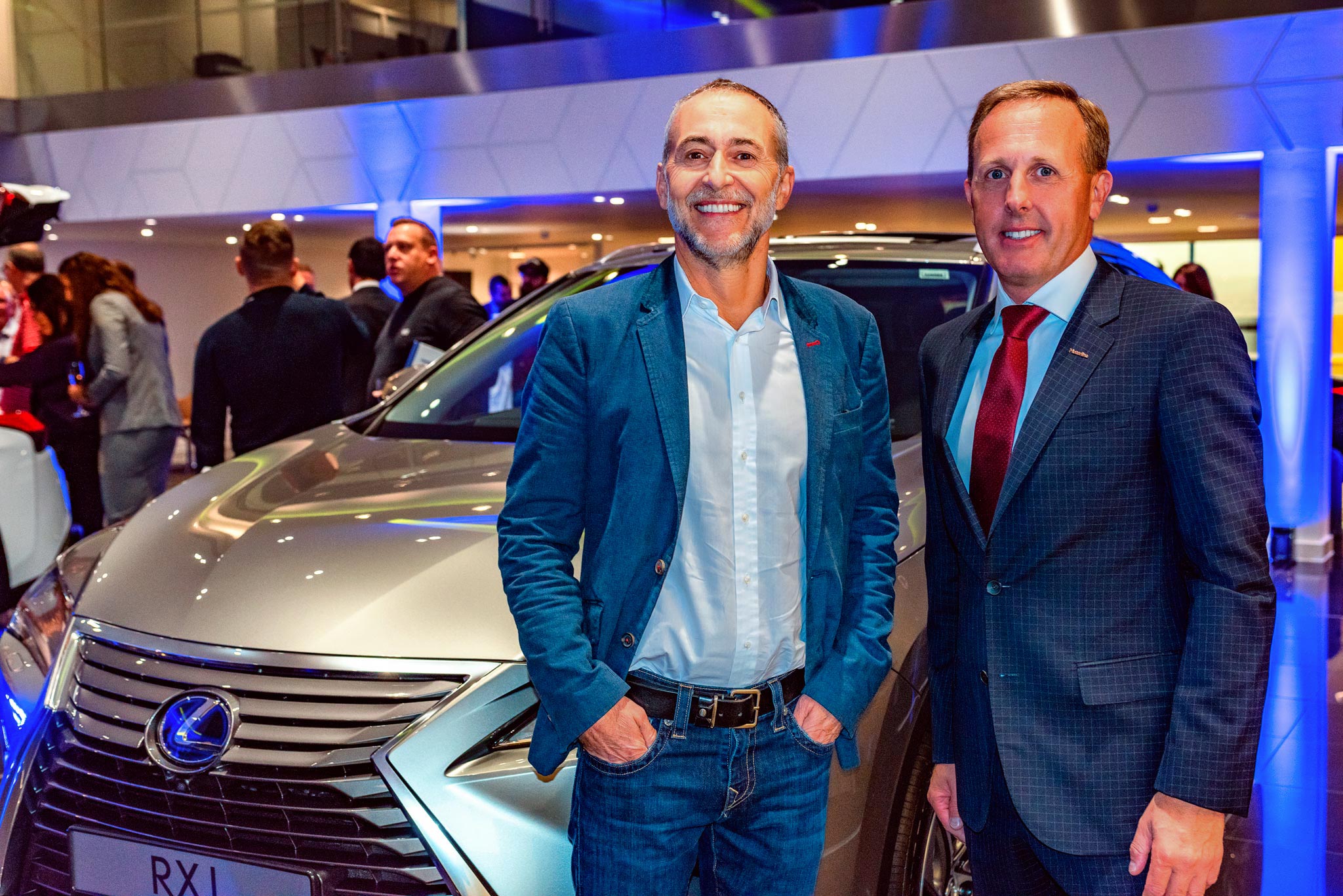 A moment captured at a corporate sales event, featuring renowned chef Michel Roux standing alongside the directors of a car showroom (Lexus). Both individuals smile at the camera, exuding enthusiasm and professionalism as they showcase a brand new Lexus model.