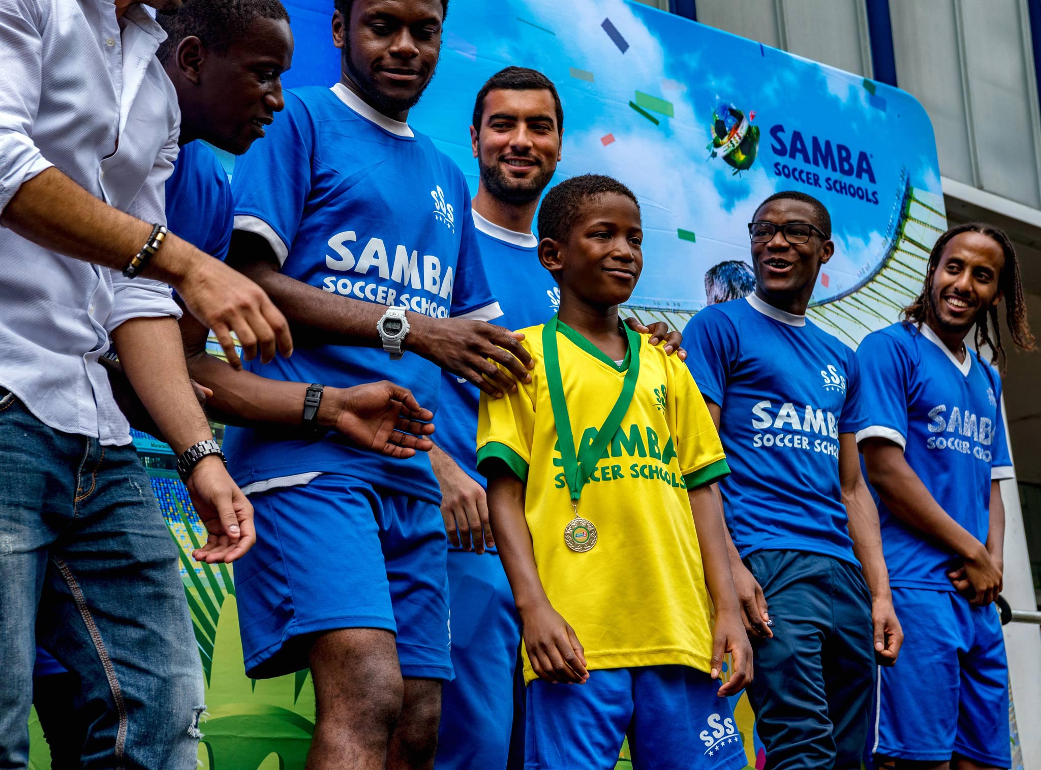 A boy receiving a medal at a football school event, standing proudly on stage in his football kit alongside his coaches.