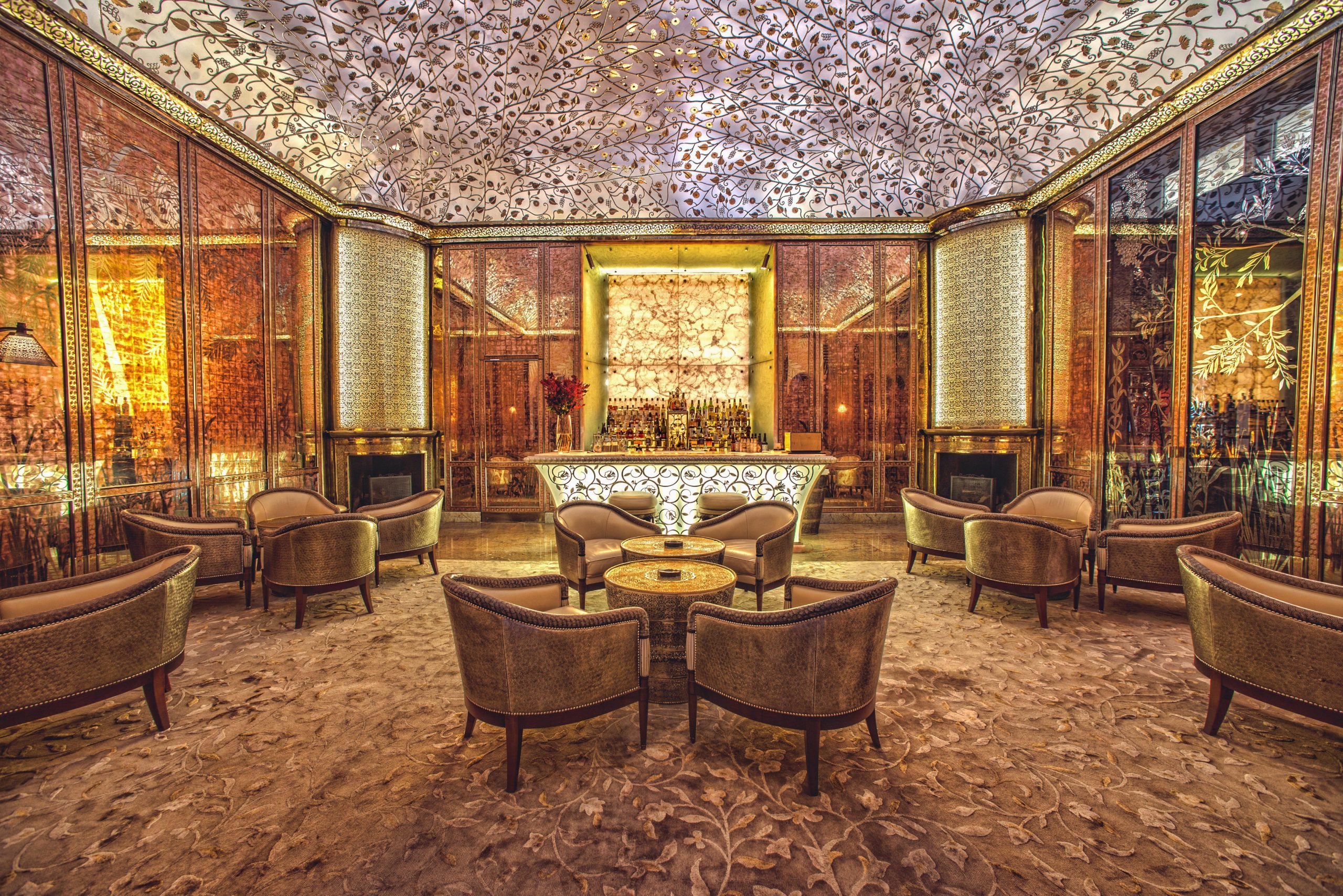 Elegant bar area in a 5-star hotel in Morocco, featuring intricate glass and metalwork ceiling, mirrored copper walls, and luxurious armchairs arranged around an aluminized bar.
