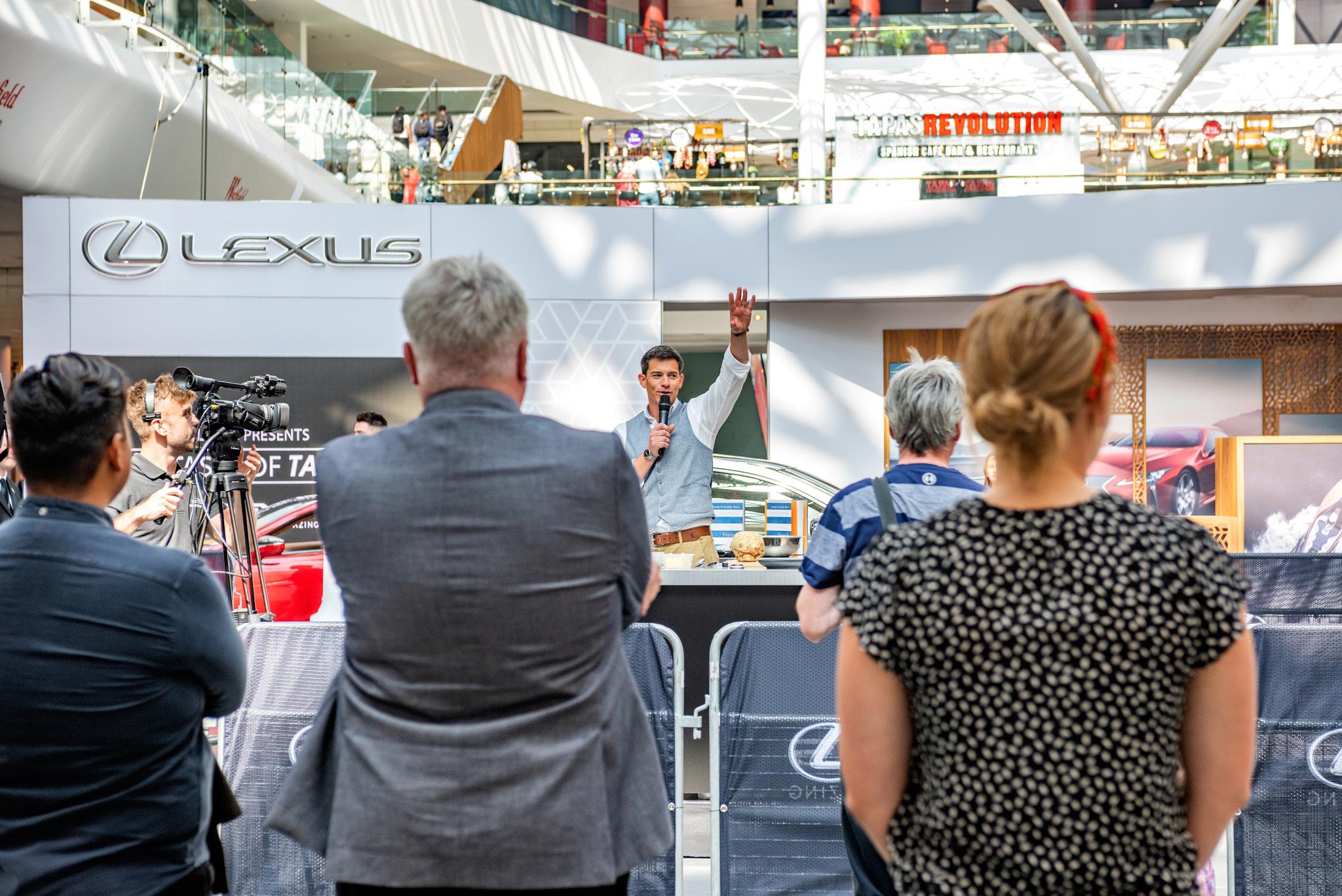 A captivating moment captured by Wright Content, showcasing Marcus Bean, a TV presenter chef, at an experiential event for Lexus. In this shot, Marcus waves to the audience while holding a microphone, adding to the excitement of the clocking demo. Wright Content specializes in production photography, expertly documenting behind-the-scenes moments like this.