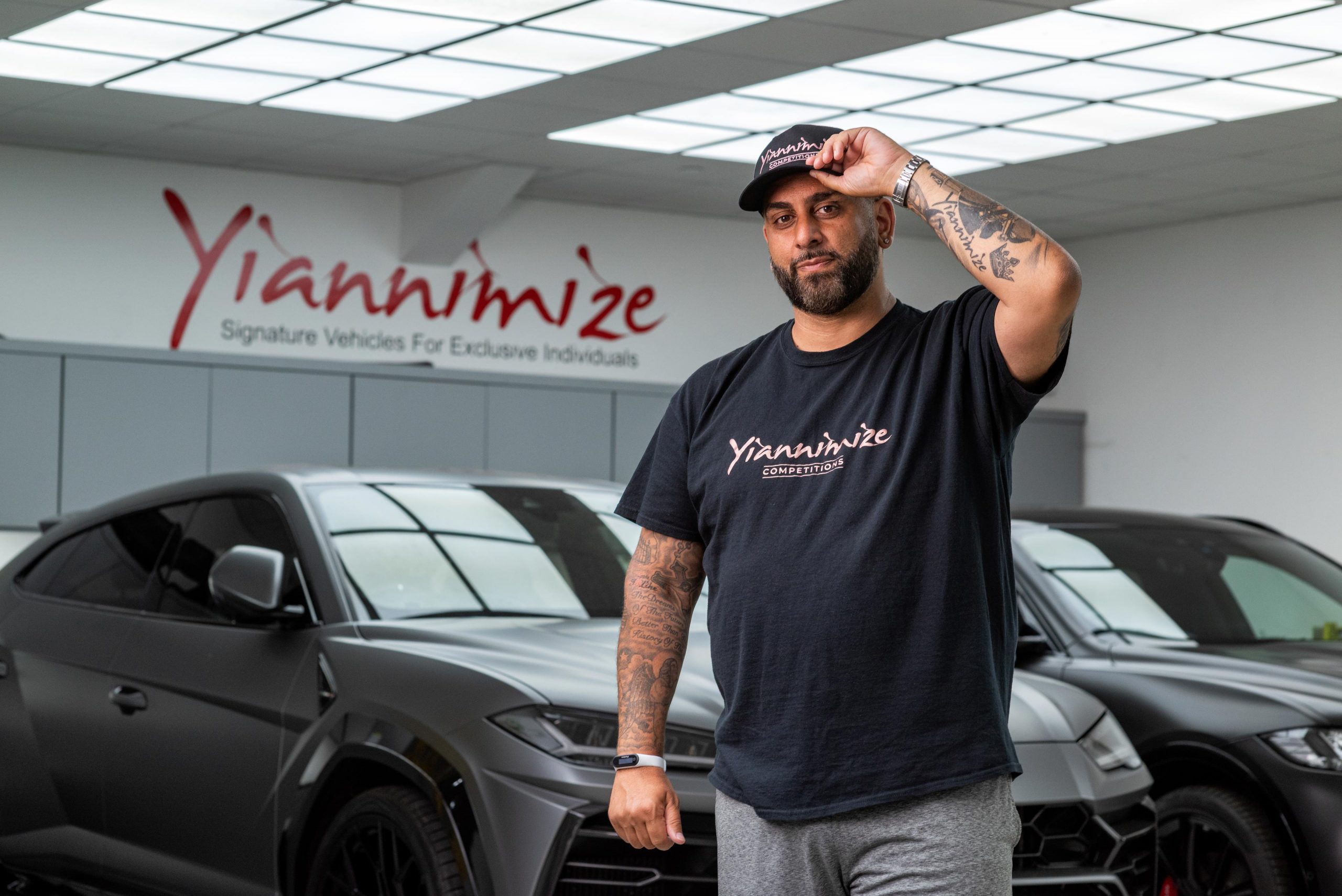 Yiannimize, the automotive enthusiast, poses in his garage with Lamborghinis in the background.